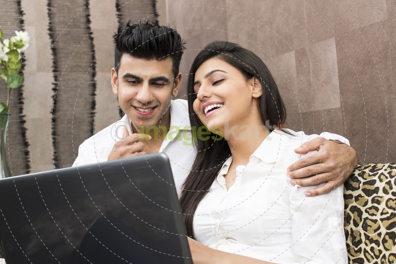 young couple laughing while browsing in laptop