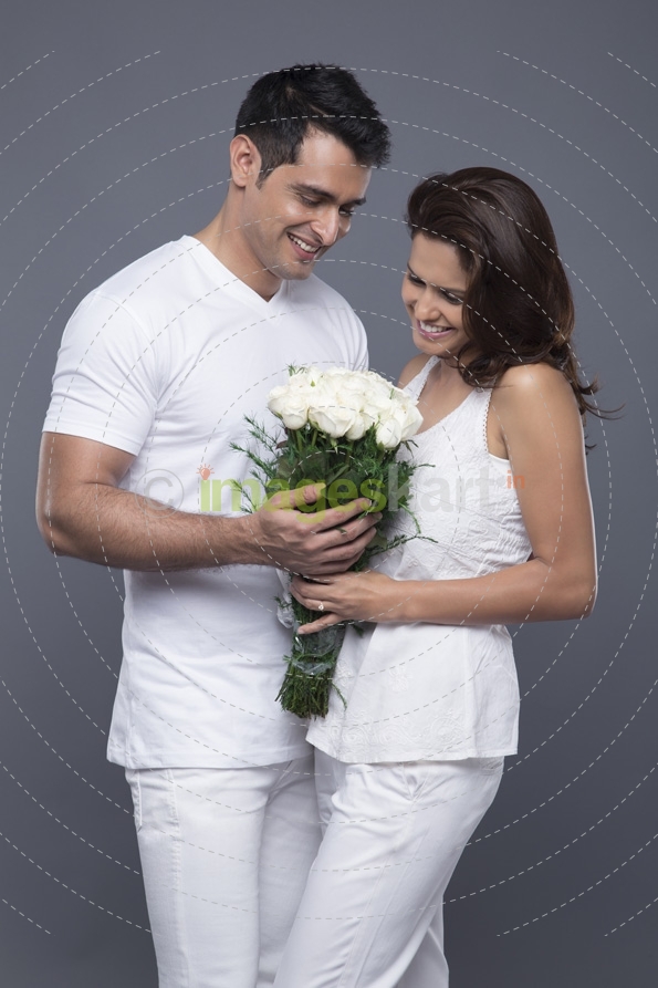 portrait of young couple in love with flowers posing against grey