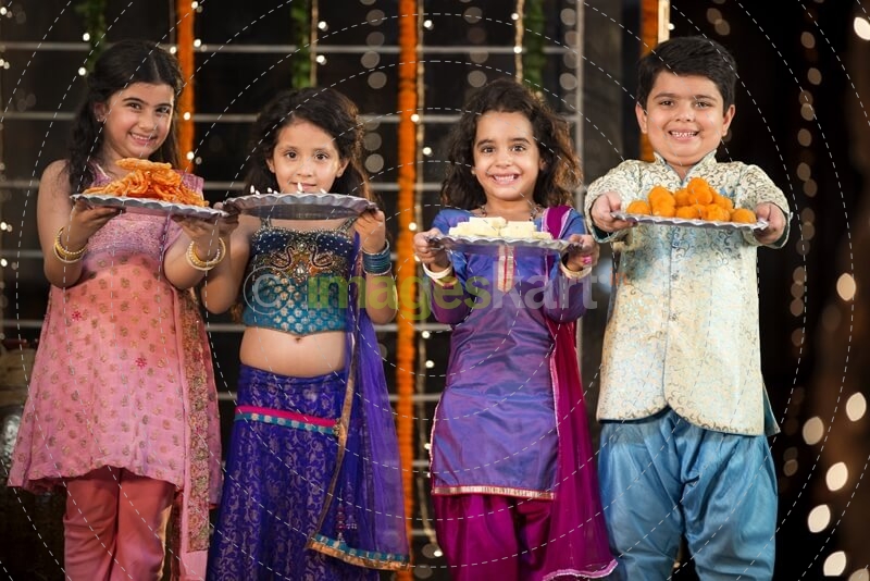 group of kids standing and offering sweets on diwali