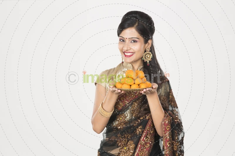 woman in saree with a plate of ladoos 