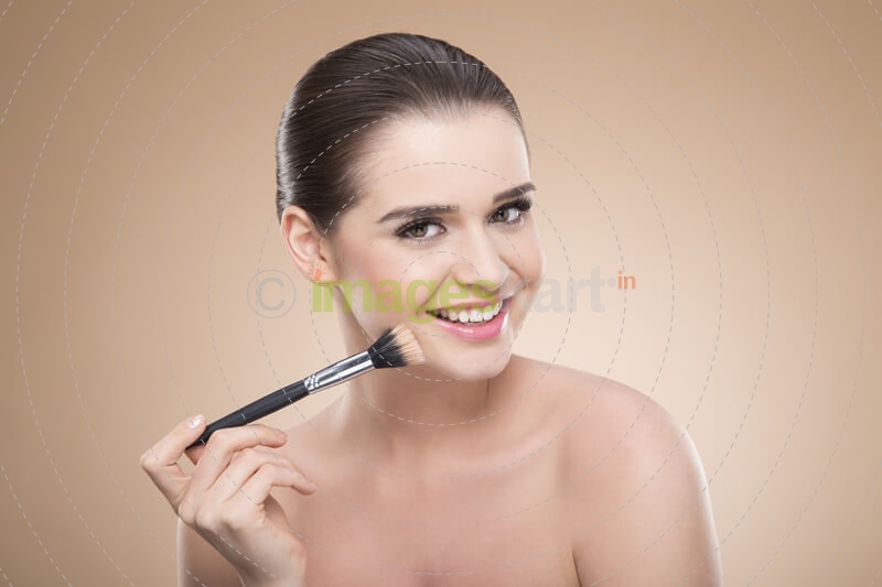 girl applying make up with brush while smiling