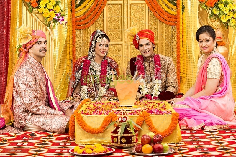 indian bride and groom sitting with parents at mandap