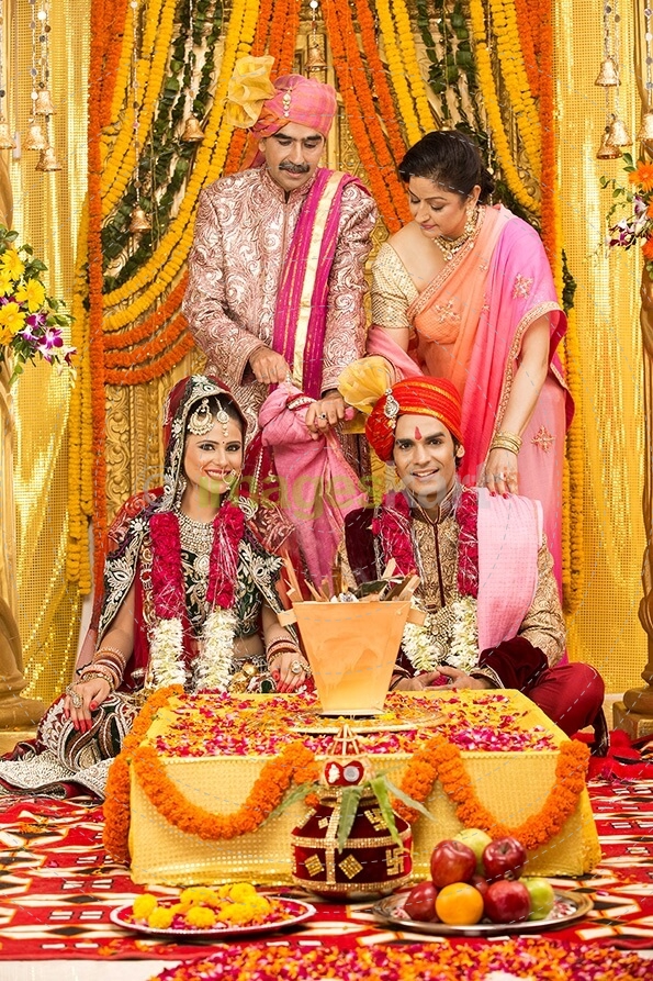 indian bride and groom sitting with parents at mandap