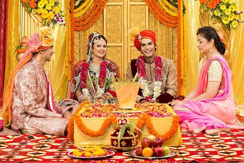 indian bride and groom sitting with parents at mandap