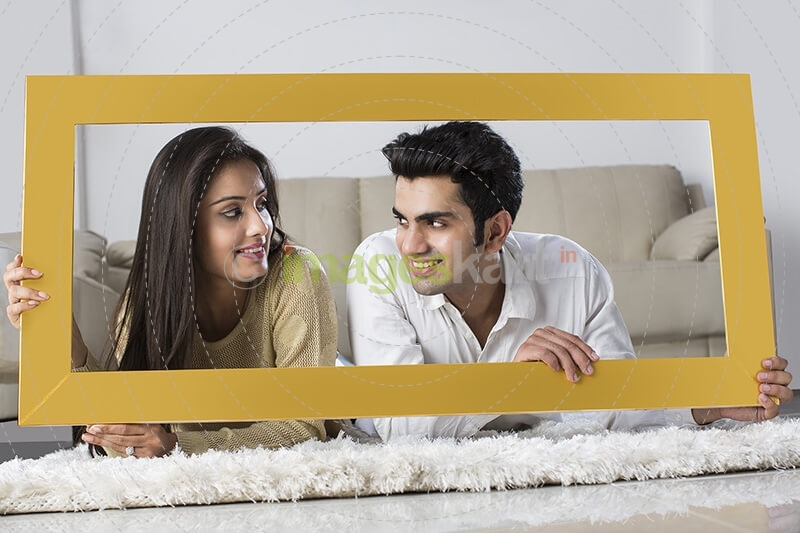 young couple posing with wooden frame at home