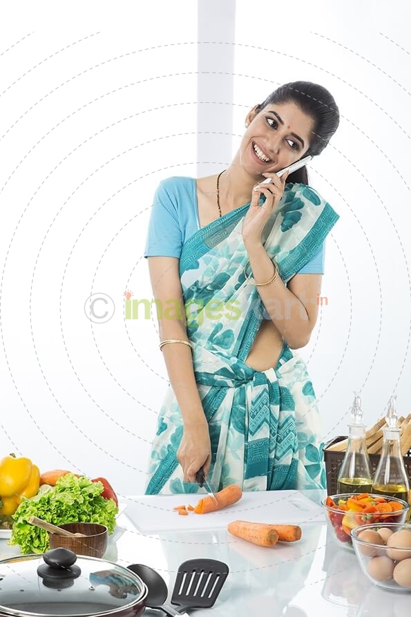 Indian housewife cutting vegetable while talking on mobile phone