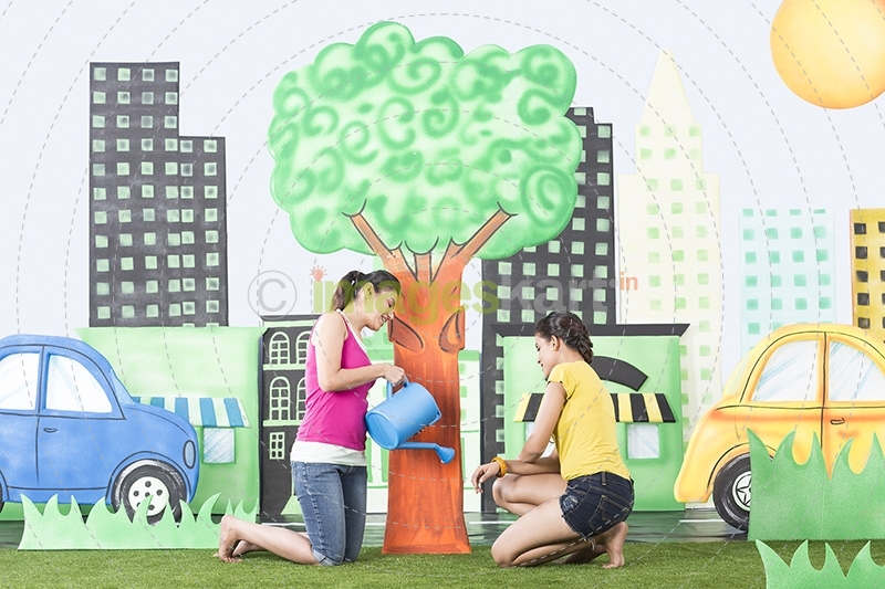 One girl watering a plant and one girl helping