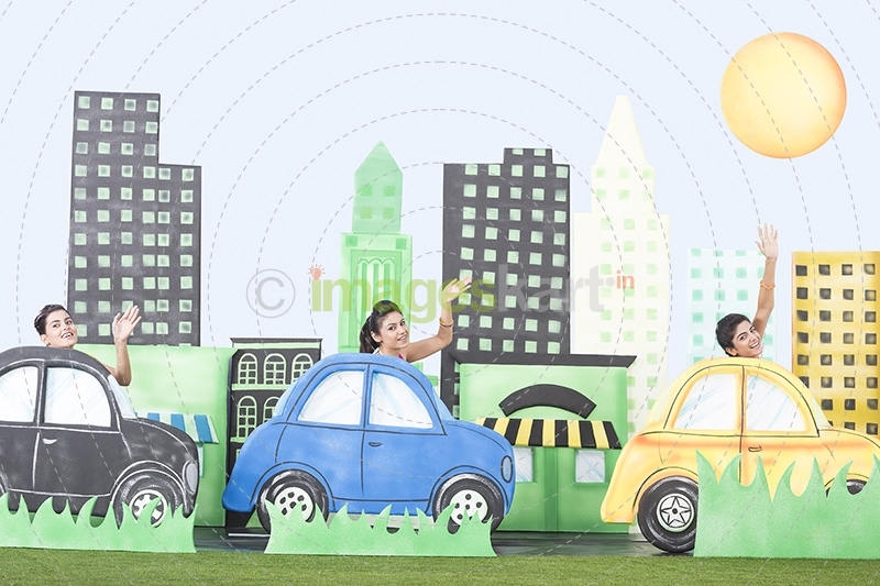 Three Girls waving hands while driving cardboard cars