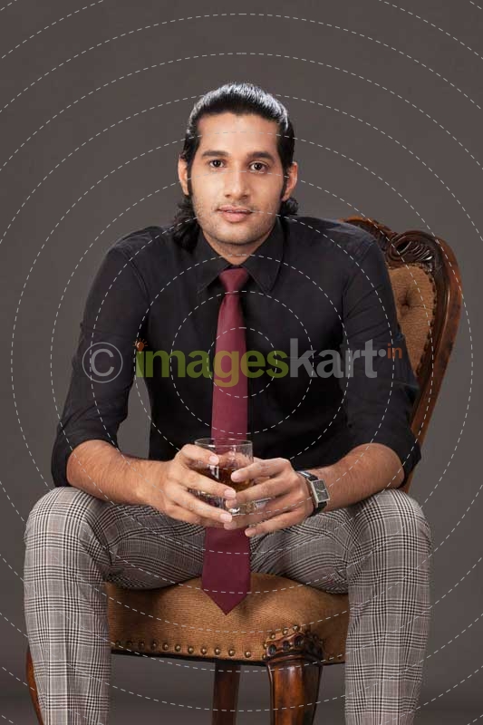 man sitting on chair while holding a drink on grey background 