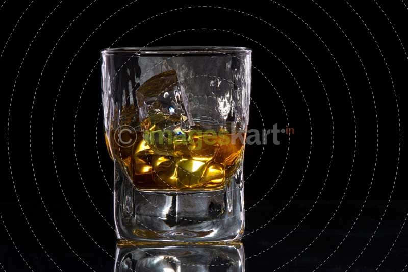 a glass of scotch with ice cubes against dark background 