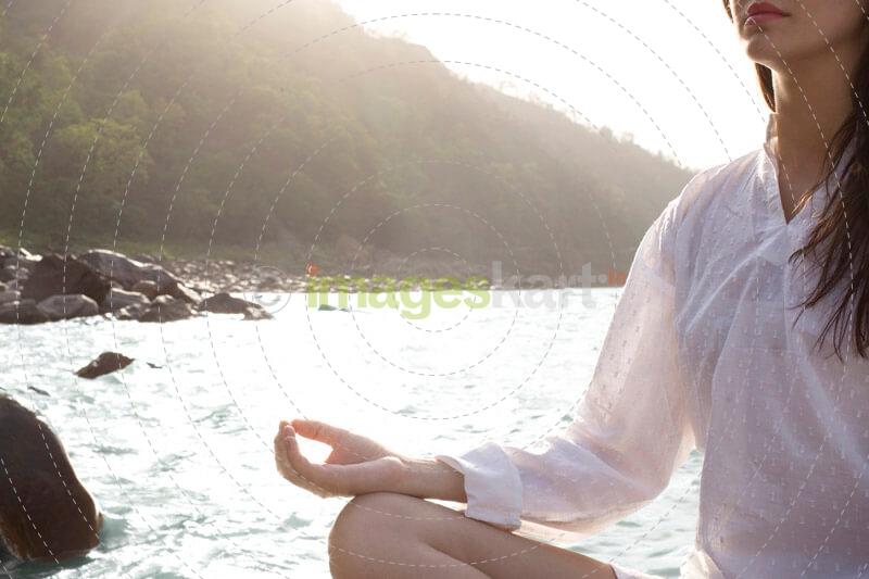 young woman meditating alongside river
