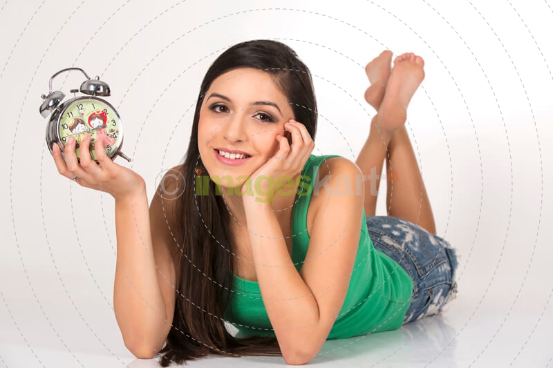 girl lying with alarm clock against white background