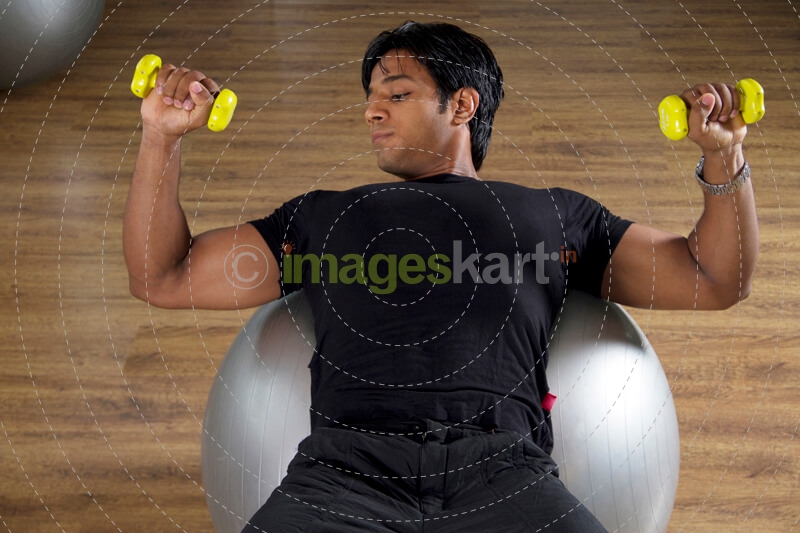strong male doing light dumbbells over a fitness ball