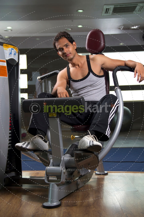 man posing with leg exercising machine at the gym