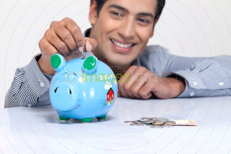 young man dropping a coin in a piggy bank