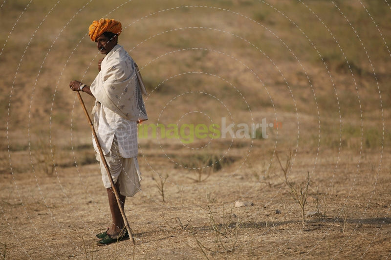 rural man walking in the field with a stick 