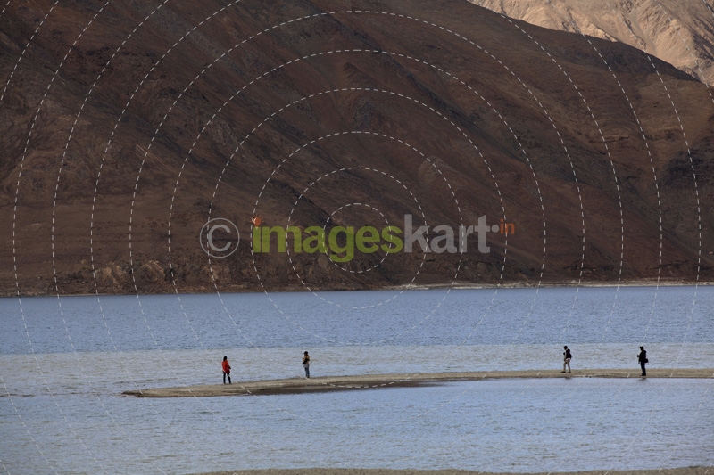 group of people standing on a river bank against a beautiful mountain 