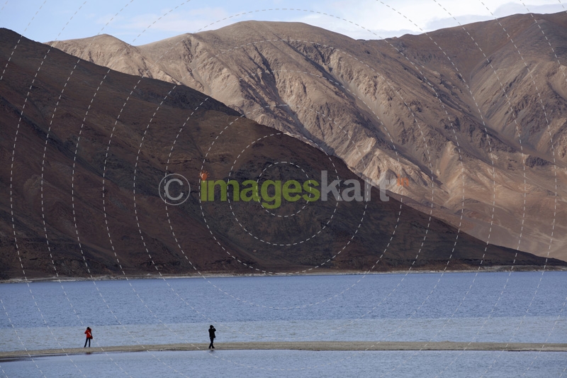 two people standing on a river bank against a beautiful mountain view