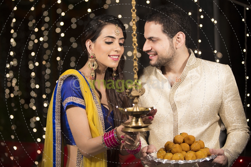 couple lighting diya and holding ladoos 