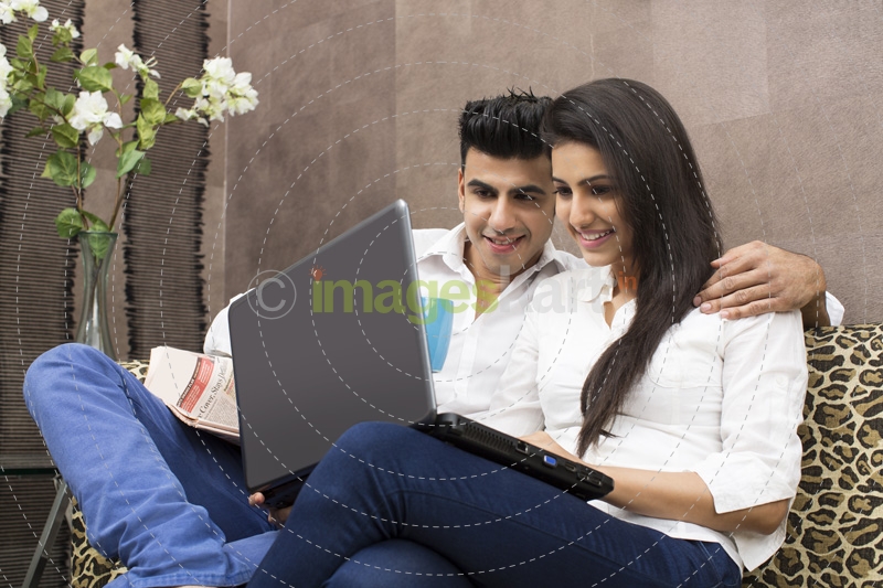couple smiling on couch while browsing in laptop
