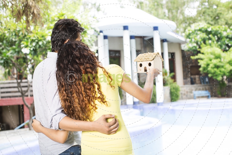 back view of the couple looking at villa while holding home miniature