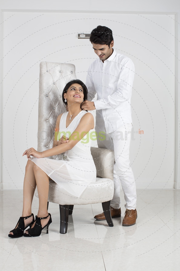 woman wears a necklace while man tying 