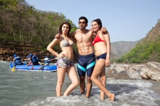 three friends posing while  men rafting in the background
