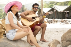 beach girl with a pink hat and funky glasses listening to the guitar