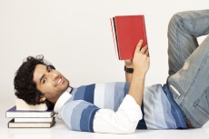 college boy lying down on pile of books 