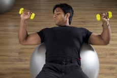 strong male doing light dumbbells over a fitness ball