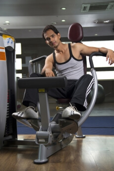 man posing with leg exercising machine at the gym