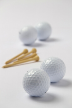 four golf balls with golf tees on white surface 