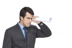 man in suit looking through rolled sheet of paper