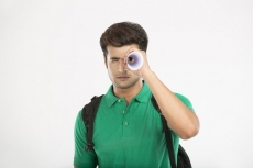 college boy looking through rolled sheet of paper 