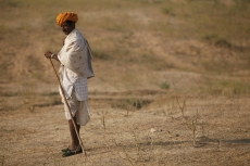 rural man walking in the field with a stick 