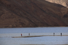 group of people standing on a river bank against a beautiful mountain 