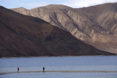 two people standing on a river bank against a beautiful mountain view