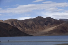 man standing on a river bank against a beautiful mountain view
