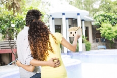 back view of the couple looking at villa while holding home miniature