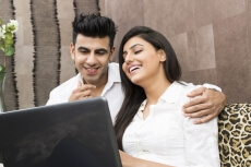 young couple laughing while browsing in laptop