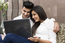 couple sitting on couch browsing on laptop