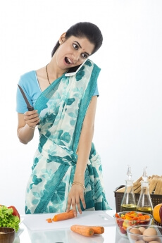 Indian housewife cutting vegetable while talking on mobile phone