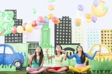 Three girls sitting on grass and floating balloons